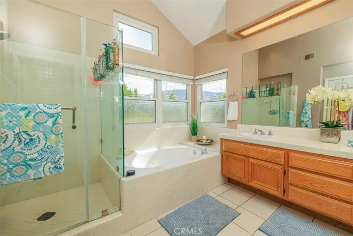 En suite primary bath features deep, soaking tub with privacy glass, separate frameless shower enclosure, double-sink vanity, and tile flooring