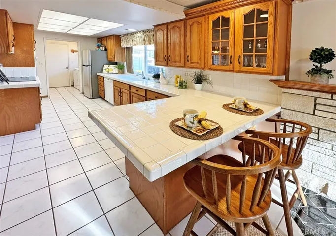 Upgraded Kitchen Boasts Tile Countertops, Wrap-Around Breakfast Bar, Custom Cabinetry with Pull-Outs and Glass Display Panels