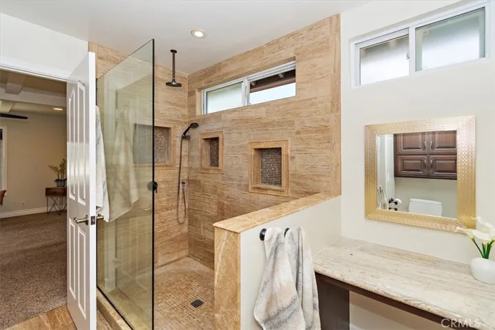At primary ensuite bathroom, luxuriate in the large floor-to-ceiling Travertine tiled walk-in shower and a personalized vanity table