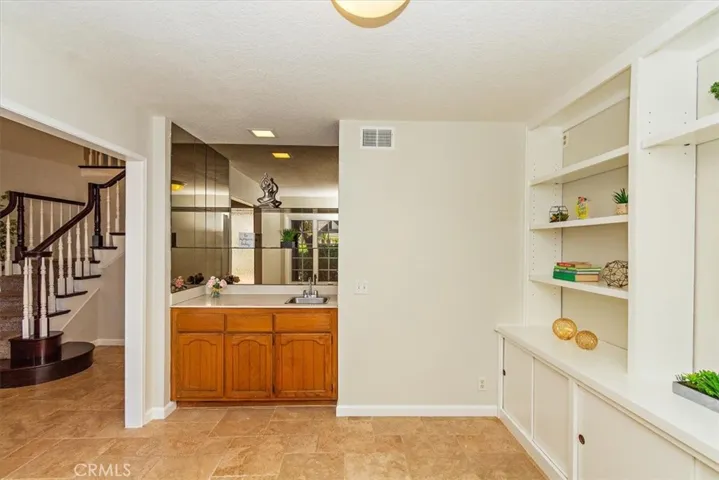 At front, a den with built-in bookshelves, a convenient hand sink, mirror walls and glass shelves offers a flexible space ideal for a home office or creative studio