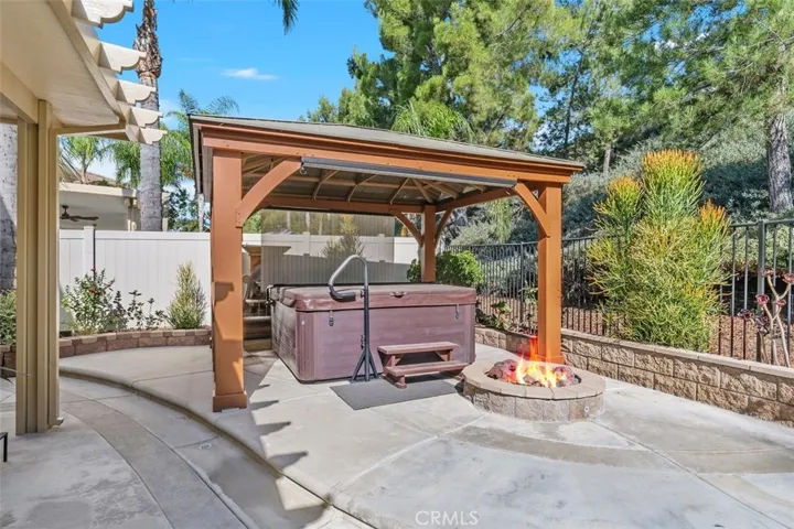 Hot tub situated under wood gazebo with shades and fire pit.