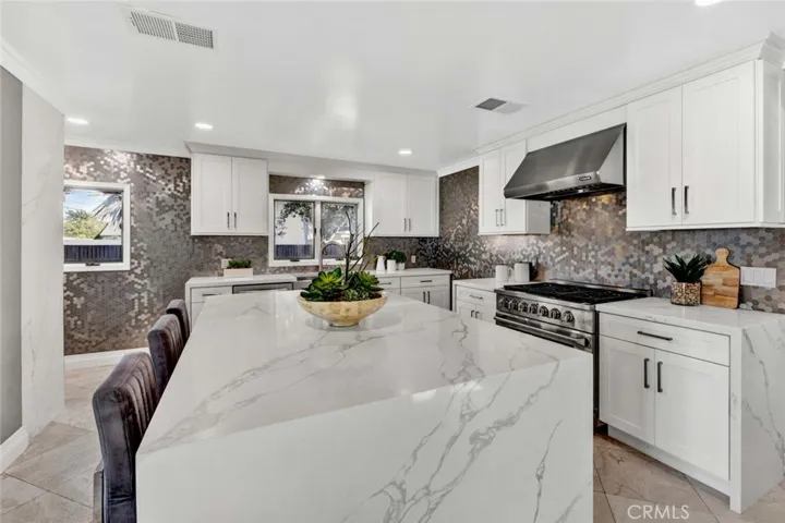 The chefs kitchen is a showstopper, complete with a spacious center island with sink, seating, and storage, along with quartz countertops, a designer backsplash and elegant white cabinetry.