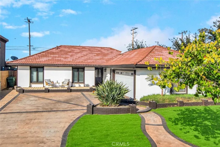 The front of the home impresses with immaculate artificial grass, a raised deck perfect for gatherings, a beautifully stained driveway with brick ribbon accents, a charming walkway, a tiled roof, and rain gutters.