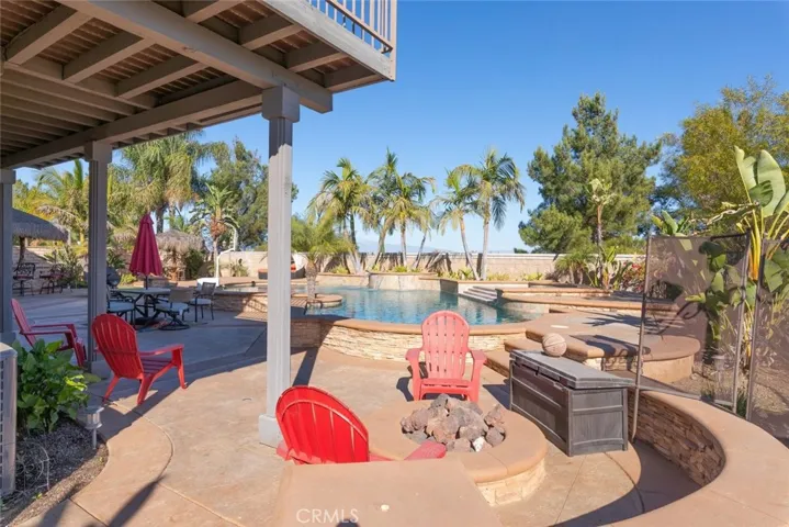 Resort-style pool and spacious entertaining area featuring a fire pit, shaded seating, and tropical landscaping.