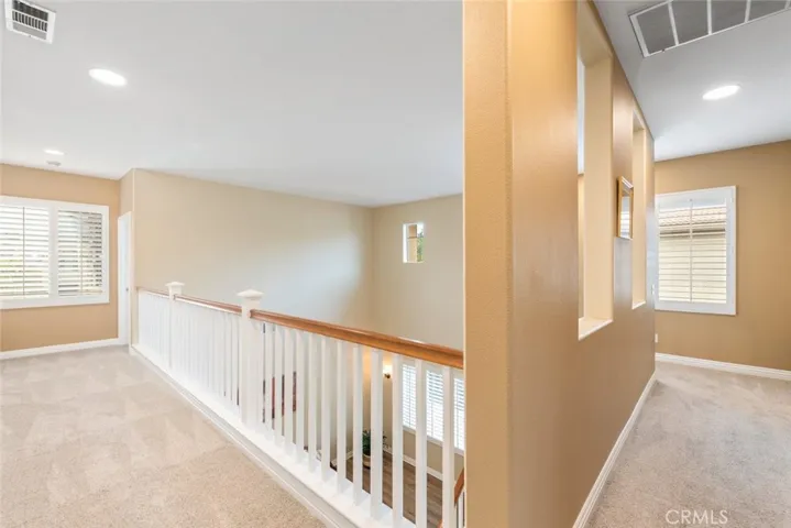 A bright and spacious upstairs landing with an open railing, and natural light for a welcoming ambiance.