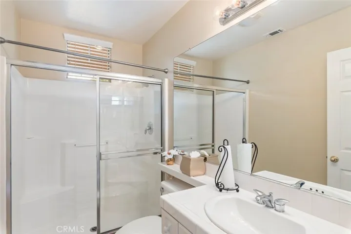 A well-lit bathroom, spacious walk-in shower,  and large vanity mirror.