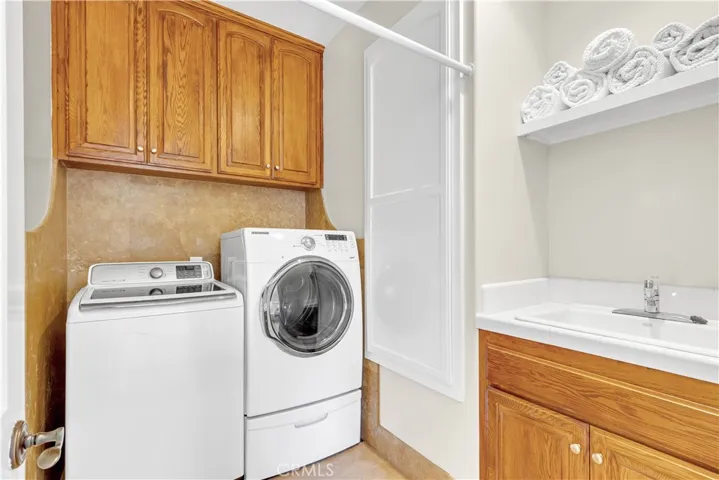 Upstairs laundry room with travertine walls and flooring is a plus with storage and a soaking sink.