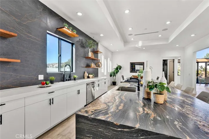 Giant leathered granite center island with seating, Quartz countertops, 2 sinks, chic floating shelving, white gloss Thermofoil self-closing cabinetry, and stainless Viking & Thermador appliances, plus coffered ceiling with recessed lighting