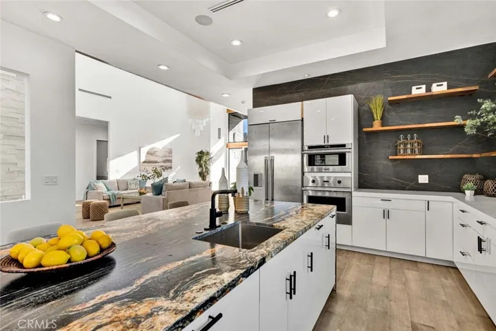 Giant leathered granite center island with seating, Quartz countertops, 2 sinks, chic floating shelving, white gloss Thermofoil self-closing cabinetry, and stainless Viking & Thermador appliances, plus coffered ceiling with recessed lighting