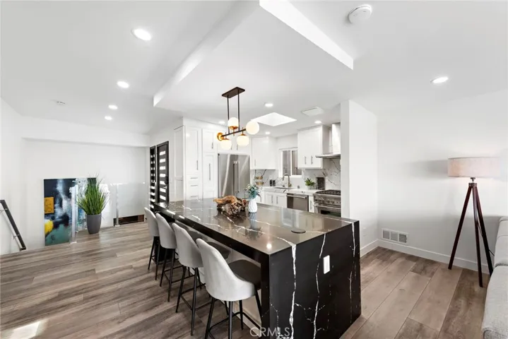 A double-waterfall island anchors the kitchen and acts as a large dining table for memorable gatherings with seating for up to six, while quartz countertops and a full backsplash are complemented by white cabinetry.