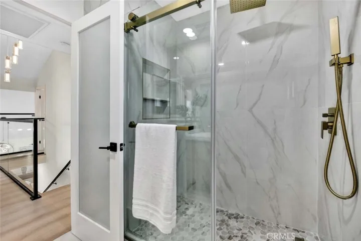 Upstairs guest bathroom has marble walk-in shower with multiple shower heads and clear glass Barn-door style enclosure