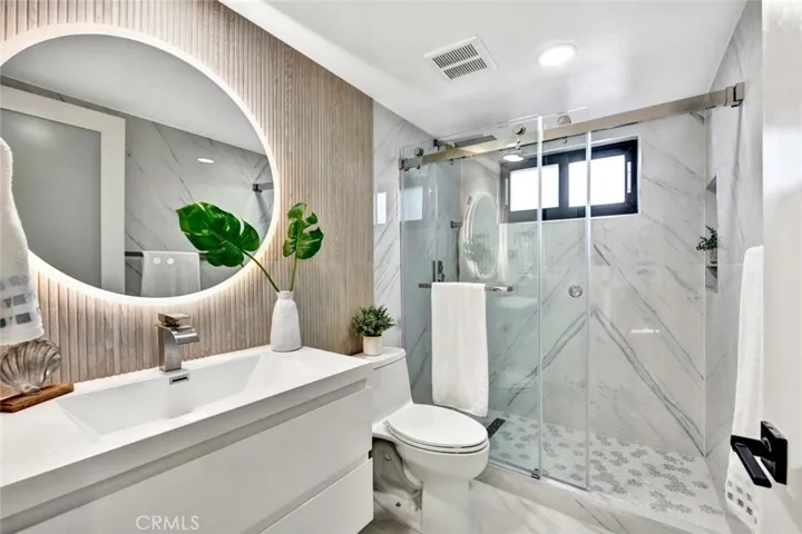 1 of 2 downstairs luxury bathrooms. Marble flooring, walk-in shower with floor-to-ceiling marble surround, clear glass barn-door style enclosure, LED touch-light-up mirrors and contemporary vanity.