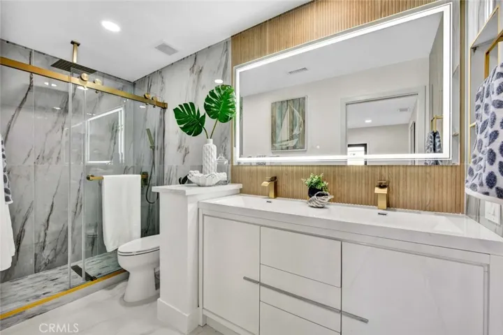  
Downstairs primary suite bathroom with contemporary vanity, dual sinks, touch-LED light-up mirror, marble flooring, walk-in shower with marble surround