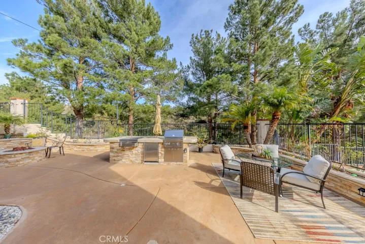 Backyard view looking to the east with pine trees gracing the slope featuring a fire pit and barbecue.
