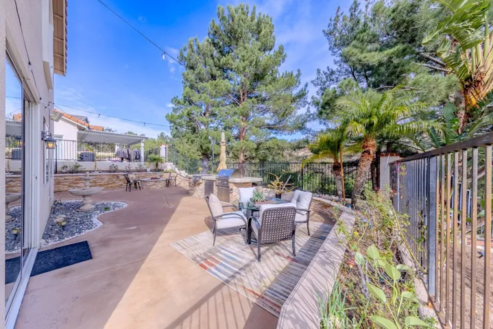 View of the backyard looking north with barbecue, fire pit, fountain, and wrought iron fencing.