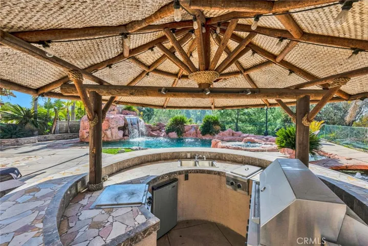 Looking inside the outdoor kitchen palapa with a view of the pool. There's a Viking barbecue and double burner, a sink and a mini refrigerator.