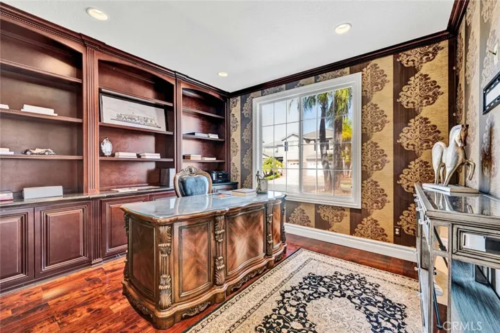 To the right from the foyer, you find this ensuite bedroom, currently used as an office with built-in cabinetry, recessed lighting and wood flooring. The crown molding in this room matches the cabinetry.