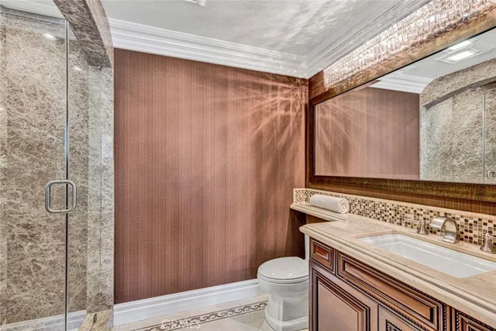 This is the ensuite bathroom with a rich wood vanity a standard commode and a walk-in shower.