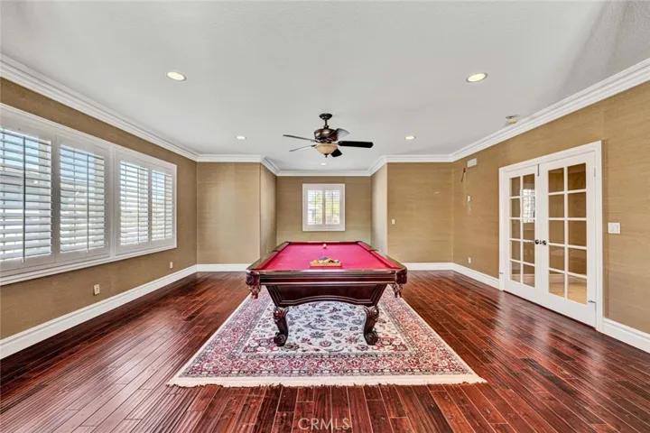 This shows almost the full length of the bonus room with rich wood flooring, recessed lighting, a ceiling fan and crown molding.