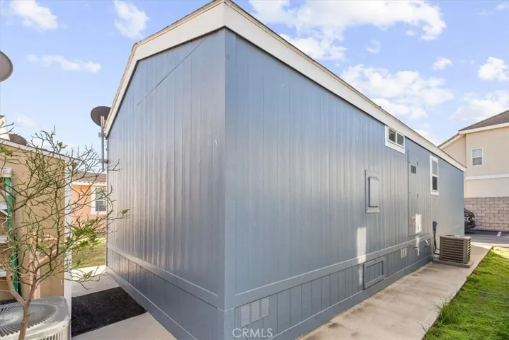 A charming manufactured home set in a well-maintained community. The home's clean, modern siding and neatly landscaped surroundings create a cozy and inviting curb appeal. Side view with AC unit.