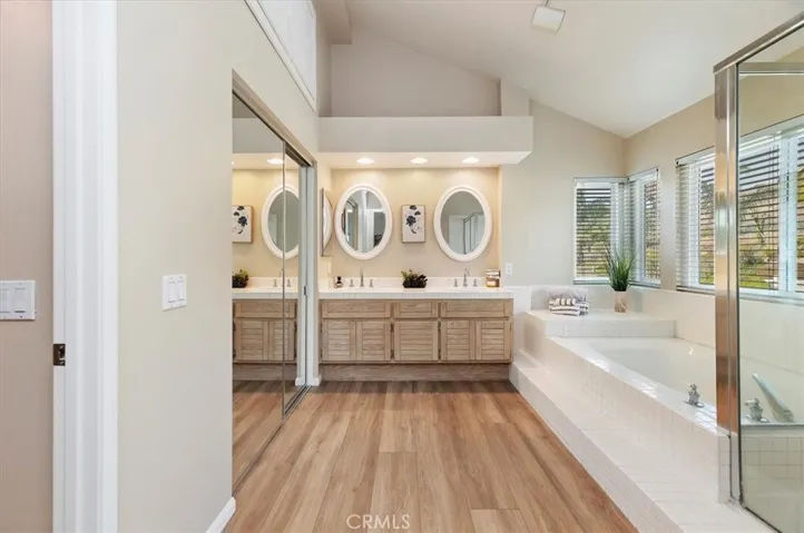 Adjoining primary bath with relaxing soaking tub and separate walk in shower. Dual pullman. With mirrored wardrobe door and spacious walk-in closet with organizer.  Vaulted ceiling. Above the closet are extra storage cabinets. Notice views from windows
