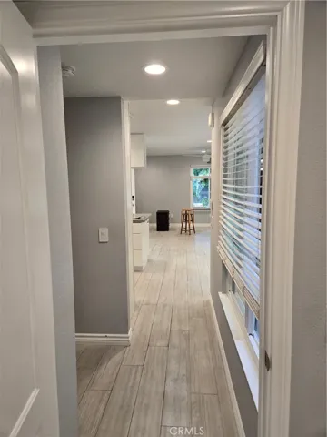 View from second bedroom down hall to living/dining/kitchen with enclosed atrium to right