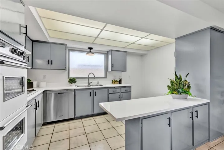 Kitchen has Newly Painted Cabinetry, Breakfast Bar, Double Ovens, Gas Cooktop with Vent Hood, Stainless Dishwasher and Sink, and Resurfaced Countertops