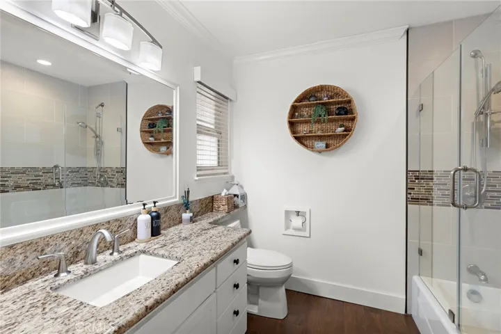 The guest bath is beautifully updated with a granite countertop, a tub/shower combo with tiled surround, and a modern frameless glass door