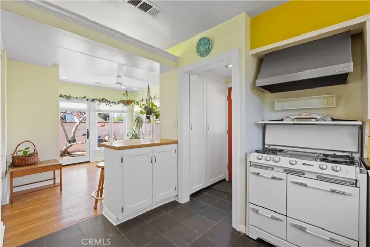 Kitchen: vintage O'Keefe & Merritt 4-burner + griddle gas range is included! Real stainless steel vent hood, pantry cabinets with vintage swing out shelving through doorway, breakfast bar, 3-tone paint scheme, view to Sun Room.

