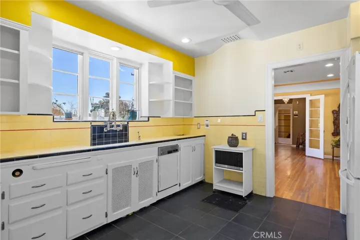 Kitchen: view to dining room, slate tile flooring, original cabinetry, 4-color original tile countertops and backsplashes, new ceiling fan, match holder, garbage chute.