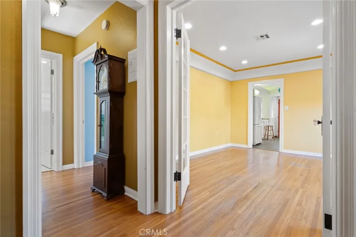 Front Entry Foyer: view to formal dining room and hallway, original hardwood flooring, french doors to dining room, glass door knobs, original period ceiling light fixture in hallway, coved & trayed ceiling in dining room with 3-toned paint scheme, wide sculpted mouldings, newer dimmable recessed can lighting, doorway to kitchen at rear.

