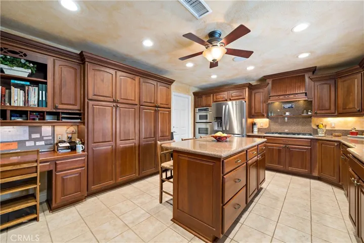 Spacious kitchen w tiled flooring, built in desk, PLENTY of cabinet space with under cabinet lighting and stainless steel appliances including fridge, oven, microwave and dishwasher and custom vented hood at gas range top