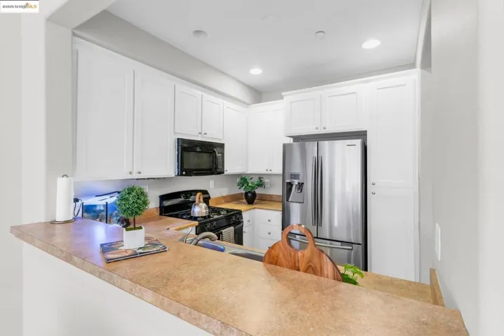 Kitchen featuring white cabinets, black appliances, light countertops, recessed lighting, and a peninsula
