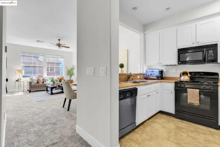 Kitchen with black appliances, light countertops, white cabinetry, ceiling fan, and open floor plan