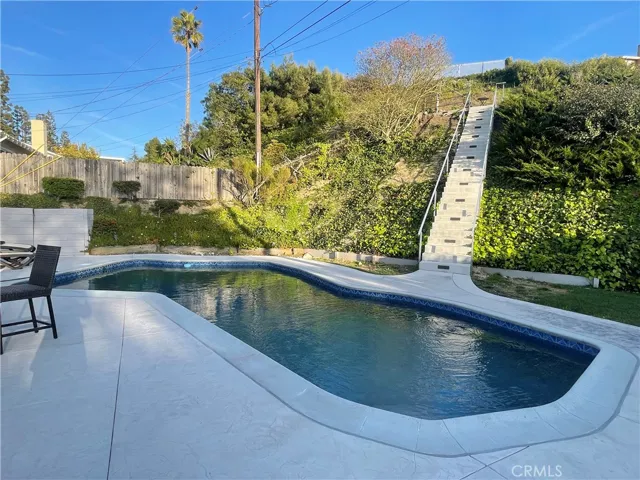 Large, private backyard with a heated pool and newly paved concrete patio, stairs, and hillside lookout.