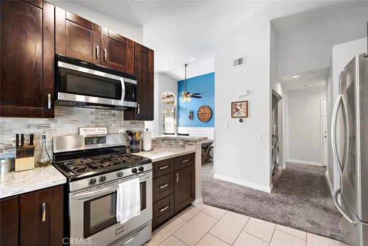 Wood cabinets , Granite counter tops , gas burner stove top. Chefs preference . Tile flooring , stainless steel appliances, right side of picture in the background is the door to the garage, laundry closet secondary bedroom.