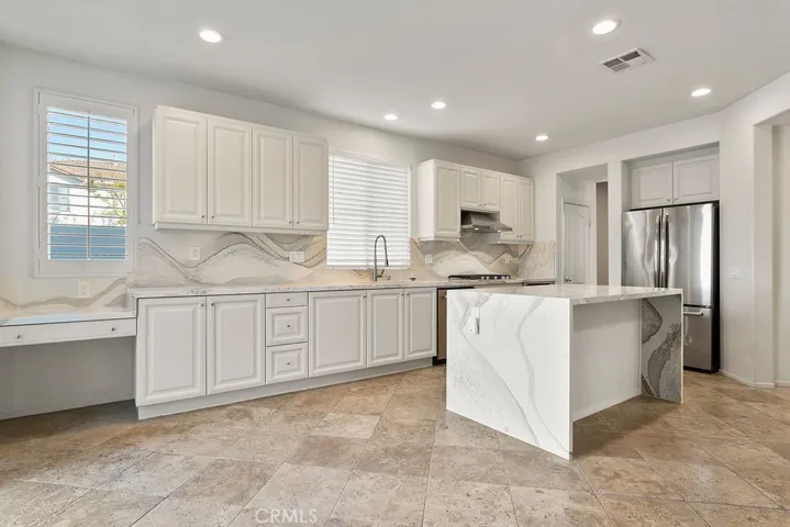 Large kitchen with white cabinets, quartz counter tops with a waterfall edge on island, travertine floors and stainless steel appliances