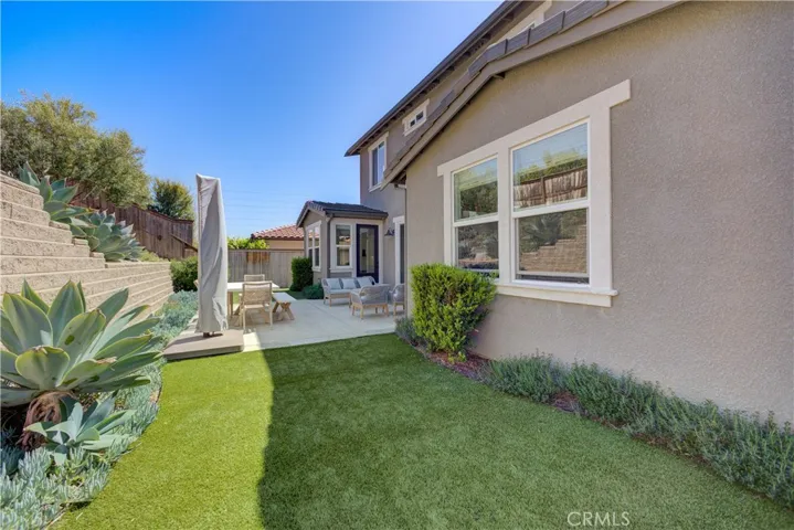 The backyard features grass on both sides of the lounging area and low-maintenance landscaping along the edges of the lawn.