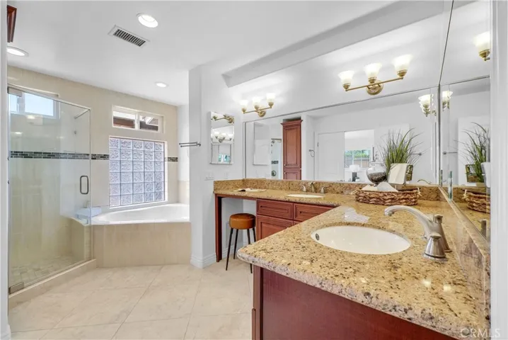 The primary spa-style bathroom featuring a dual-sink wrap-around vanity w/sit-down area, jetted soaking tub, and a separate shower