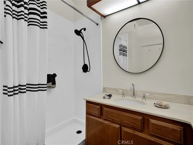 Spacious en suite master bathroom featuring dual sinks, updated circular mirrors, and a newly remodeled, walk-in style shower with modern tile and black hardware.