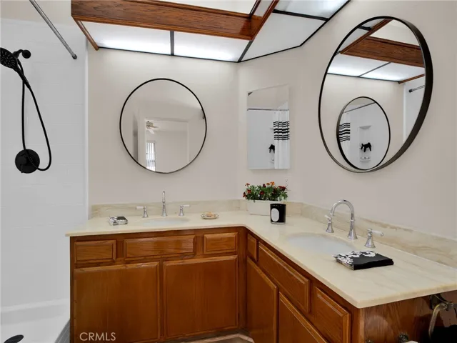 Spacious en suite master bathroom featuring dual sinks, updated circular mirrors, and a newly remodeled, walk-in style shower with modern tile and black hardware.