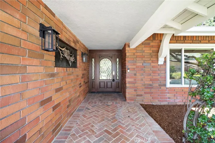 Step into timeless charm through a classic brick entryway with herringbone pavers and a beautifully detailed wood door framed by leaded glass panels.
