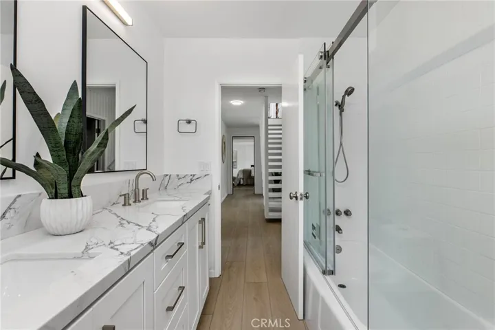 Downstairs bathroom remodeled with quartz countertops, custom cabinets, dual sinks, and glass enclosed shower and tub.