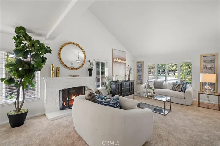 The formal living room is filled with natural light from large windows and highlights plantation shutters and soaring vaulted ceilings.