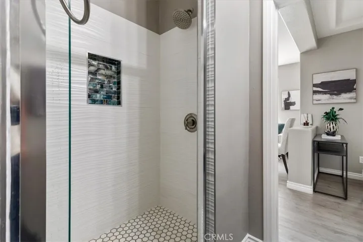 The modern walk-in shower features elegant tile detailing and a built-in niche, while the dark wood vanity and framed mirror add a touch of sophistication.
