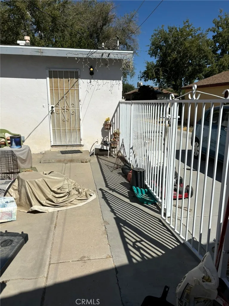 Rear view of home showing back entrance, paved patio area, and wrought iron fence separating driveway access.