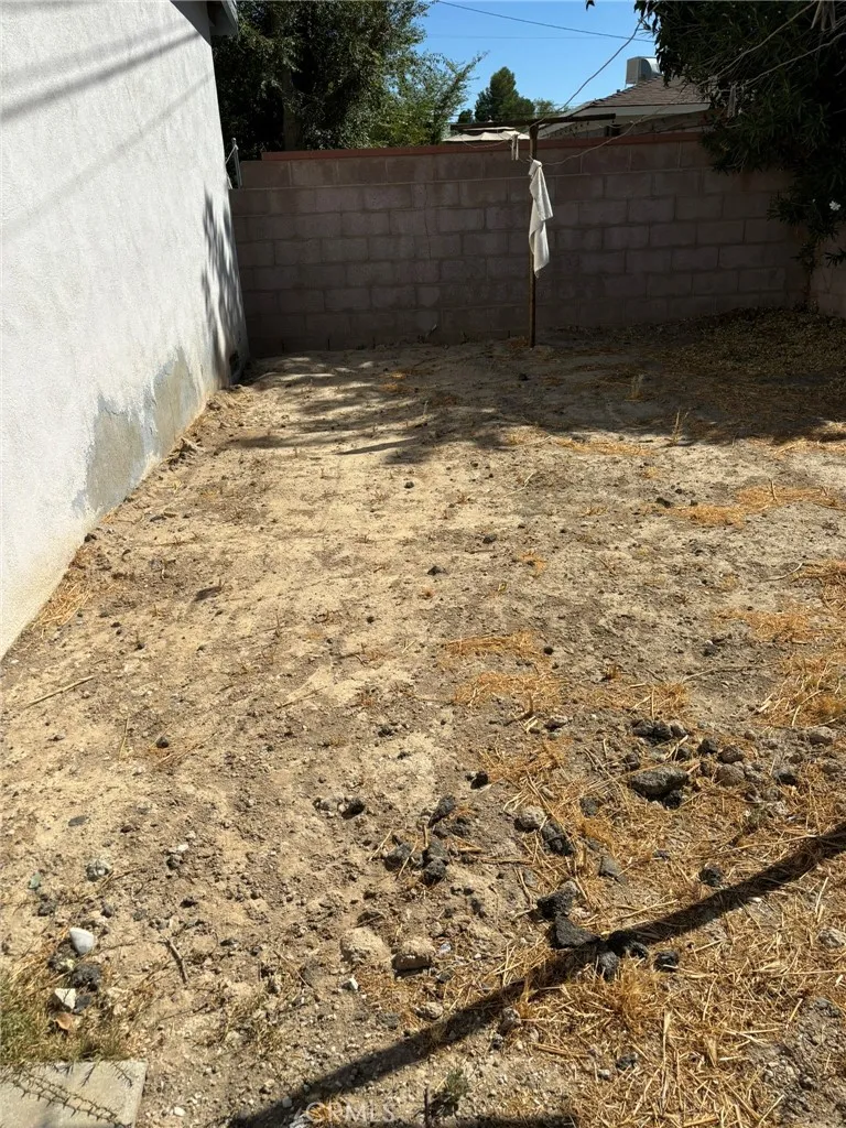 Side portion of backyard adjacent to garage, with block wall fencing and open dirt area suitable for garden or additional use.