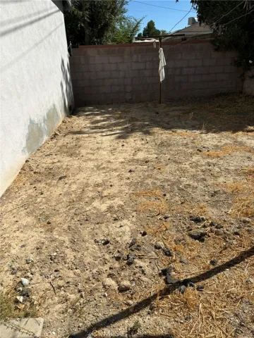 Side portion of backyard adjacent to garage, with block wall fencing and open dirt area suitable for garden or additional use.
