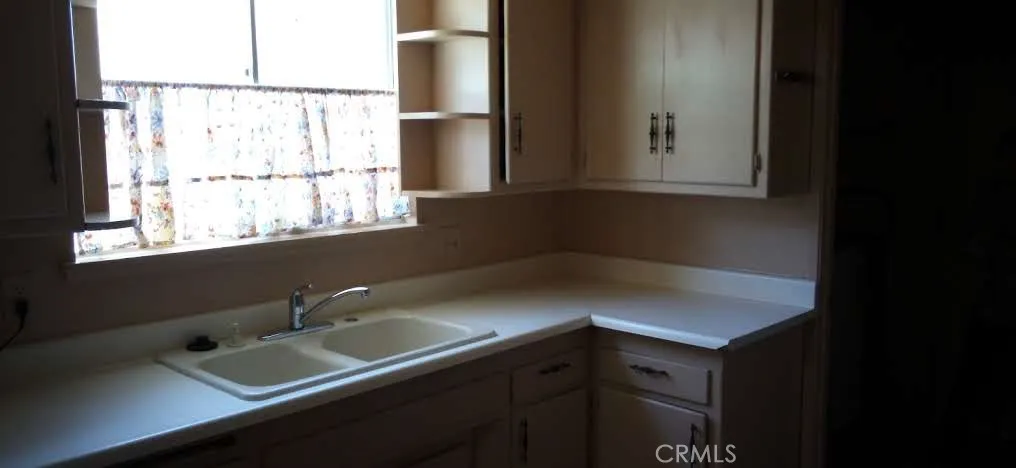 Double-basin kitchen sink with older cabinetry and decorative window shelf.