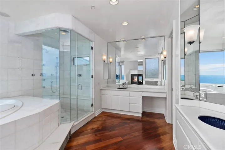 The shower and tub of this primary bathroom are all done in white marble stone, as ar the counter at both sinks.